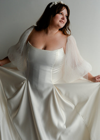 Designer Kathryn bass wearing a the poppy/laura bridal gown with a structured bodice and pleated skirt,. Shown here with the audrey pleated balloon sleeves.