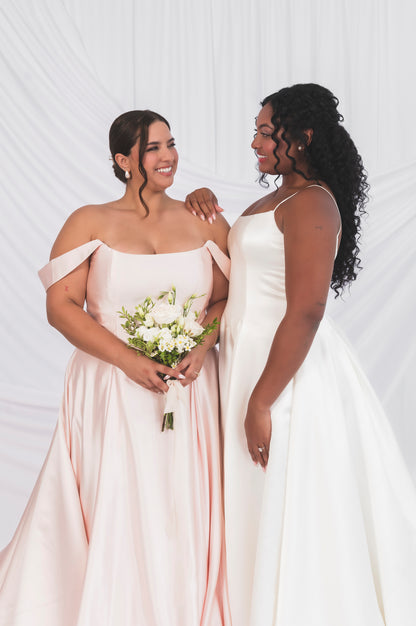 Two versions of the poppy/laura wedding dress. The plus size bride in Ottawa is wearing the blush satin version with matching off the shoulder drapes and our other bride is wearing the poppy/laura in ivory with a narrow strap.