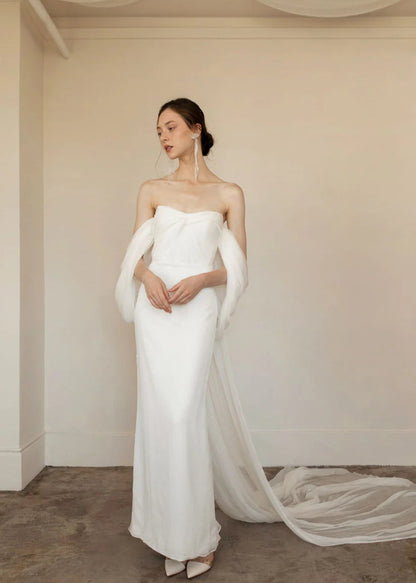 Priscilla is sleek, chic and the picture of elegance. This sheath dress is made up of crinkled chiffon and a draped bodice. Dramatic off the shoulder details and a flowy long detachable cape finish the look with perfection.