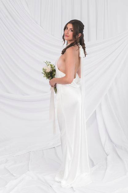 Bride in a high neck halter wedding dress holding a bouquet against a white draped curtain background