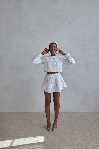Cropped long sleeve texture bridal jacket with a matching flared mini skirt against a neutral background