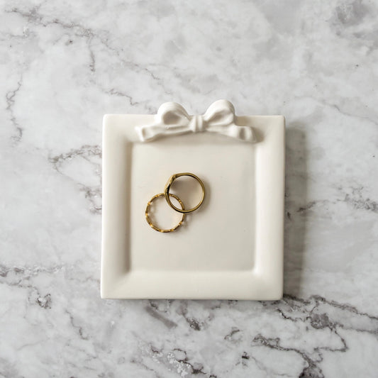 Square Jewelry Dish with a bow on top showing holding two rings on a marble countertop