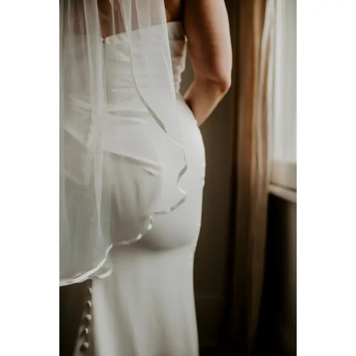 Model wearing a fingertip length satin trim veil
