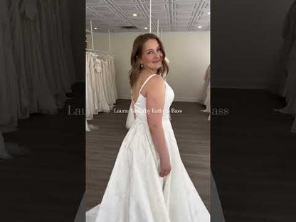 Plus Size Bride wearing the Laura/Tasha, a textured simple Aline gown featuring a narrow strap, v neck bodice, and lighweight, but full aline skirt. She is standing in front of a draped background in Ottawa Canada
