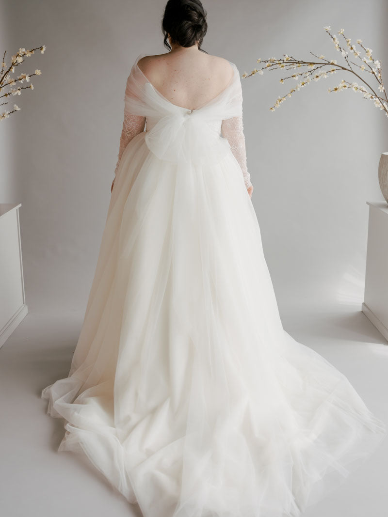 White wedding dress with sheer sleeves on a plain background